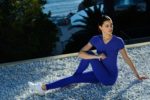 Une mannequin en tenue de sport bleue est assise sur des galets blancs dans un décor extérieur, magnifiquement capturé par le photographe Thomas Duclert. Elle étire une jambe tout en pliant l'autre genou et en tournant son torse sur le côté. L'arrière-plan présente de la verdure et un aperçu d'un plan d'eau, rappelant les lieux sereins de Paris.
