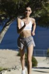 Une mannequin fait du jogging en plein air près d'un plan d'eau à Paris. Elle porte un soutien-gorge de sport blanc, un short gris et des baskets blanches. Capture par le talentueux photographe Thomas Duclert, l'arrière-plan comprend des arbres et une balustrade au bord de l'eau.