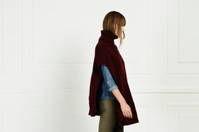 Une mannequin aux cheveux longs se tient de profil devant un mur blanc uni. Elle porte un pull à col roulé marron oversize, une chemise en jean en dessous et un pantalon vert olive. L'arrière-plan est minimaliste et épuré, mettant en valeur la tenue de la personne, une photo parfaite pour tout photographe de mode parisien.