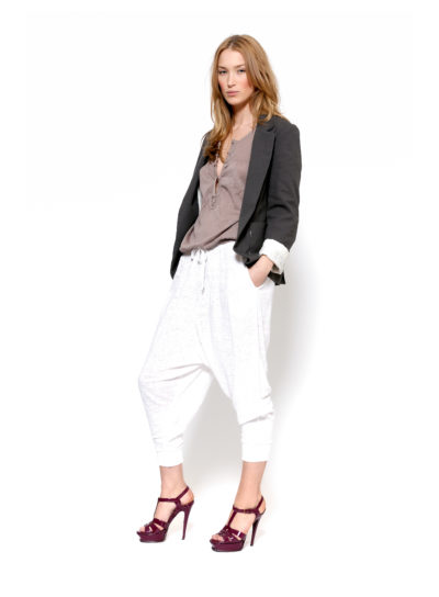 Une mannequin pose devant un fond blanc. Elle porte un blazer noir, un haut taupe, un pantalon blanc ample et des sandales à talons hauts bordeaux. Ses mains sont dans les poches de son pantalon et elle regarde l'objectif avec assurance, incarnant l'essence chic de Paris telle que capturée par le photographe Thomas Duclert.