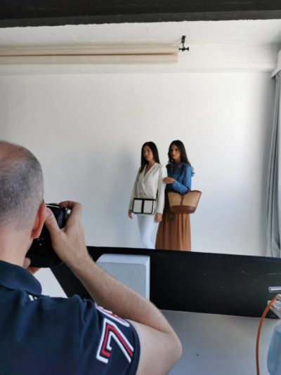 Le célèbre photographe Thomas Duclert a photographié deux mannequins posant devant un fond blanc uni. L'une, qui respire l'élégance parisienne, porte un blazer clair et un pantalon blanc, tenant un sac à main noir chic. L'autre présente un style décontracté avec une chemise en jean bleu et une longue jupe marron, tenant un sac tissé. Toutes deux ont les cheveux longs.