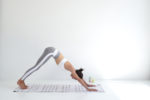 Thomas Duclert a immortalisé un moment serein à Paris, où une mannequin réalise un chien tête en bas sur un tapis rayé dans une pièce lumineuse et minimaliste. Vêtue d'un soutien-gorge de sport blanc et d'un legging gris, sa pose respire la tranquillité et la concentration.