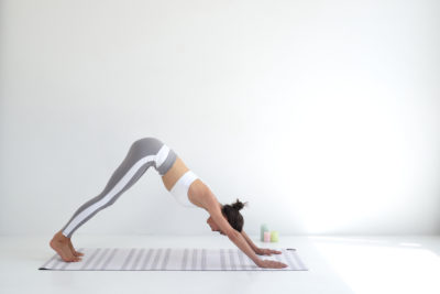 Thomas Duclert a immortalisé un moment serein à Paris, où une mannequin réalise un chien tête en bas sur un tapis rayé dans une pièce lumineuse et minimaliste. Vêtue d'un soutien-gorge de sport blanc et d'un legging gris, sa pose respire la tranquillité et la concentration.