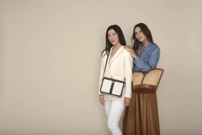 Deux mannequins posent devant un fond beige. Celle de gauche a de longs cheveux noirs, porte un blazer blanc et porte un sac noir et blanc. Celle de droite a de longs cheveux bruns, porte une chemise en jean bleu et une jupe marron et tient un sac tissé. Photo prise par le photographe parisien Thomas Duclert.