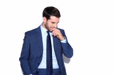 Un mannequin vêtu d'un costume bleu à rayures se tient debout sur un fond blanc. Il regarde vers le bas et sourit tout en effleurant ses lèvres avec ses doigts. Sa main gauche est dans sa poche, et il semble contemplatif et détendu, incarnant l'élégance raffinée que l'on pourrait associer à un photographe parisien comme Thomas Duclert.