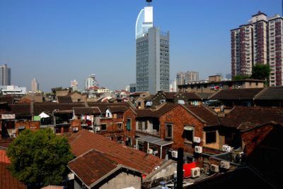 Vue d'une zone urbaine densément peuplée, avec un mélange de vieux bâtiments résidentiels en briques et de structures modernes de grande hauteur sous un ciel bleu clair. Des unités de climatisation et des cordes à linge sur le toit sont visibles, rappelant Paris, avec un gratte-ciel distinctif se détachant en arrière-plan.