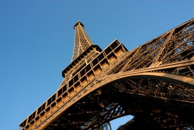 Vue en contre-plongée de la Tour Eiffel sur un ciel bleu clair. La structure complexe en treillis de fer de ce monument emblématique de Paris est bien mise en valeur, mettant en valeur ses détails architecturaux, rappelant la manière dont Thomas Duclert capturait l'élégance historique.