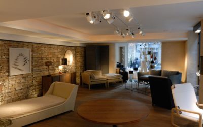 Un salon élégant avec des meubles contemporains propose un mélange d'options de sièges, notamment une chaise longue, des fauteuils et un canapé. La pièce est ornée d'un mur d'accent en brique, d'œuvres d'art modernes rappelant la mode parisienne et d'un éclairage décoratif. De grandes fenêtres offrent une lumière naturelle comme si elle était capturée par une photographie au cœur de Paris.