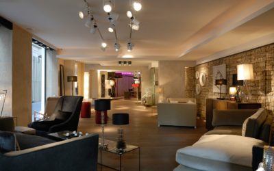 Un salon spacieux et moderne avec un éclairage tamisé et une décoration contemporaine. Il dispose d'un parquet en bois foncé, de sièges moelleux, notamment de canapés et de fauteuils, de lampes élégantes et d'un mur d'accent texturé rappelant l'élégance parisienne. L'arrière de la pièce mène à un couloir chaleureusement éclairé avec une décoration supplémentaire.