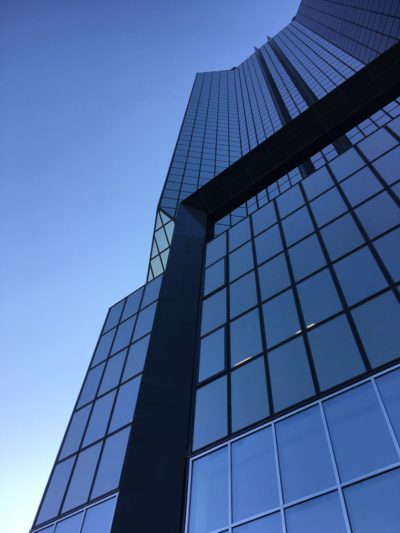 Vue en contre-plongée d'un immeuble moderne de grande hauteur avec des fenêtres en verre réfléchissant et des lignes verticales sombres, rappelant la mode sophistiquée de Paris. Le ciel bleu clair contraste magnifiquement avec le design épuré du bâtiment.