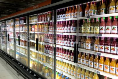 Dans un supermarché, le rayon des jus de fruits réfrigérés est entièrement approvisionné avec différents types et marques de jus. Les étagères sont remplies de jus d'orange, de jus de pomme et d'autres jus de fruits dans des bouteilles en plastique transparent et en verre, soigneusement rangées derrière des portes vitrées. C'est une scène digne d'une exposition de Thomas Duclert à Paris.